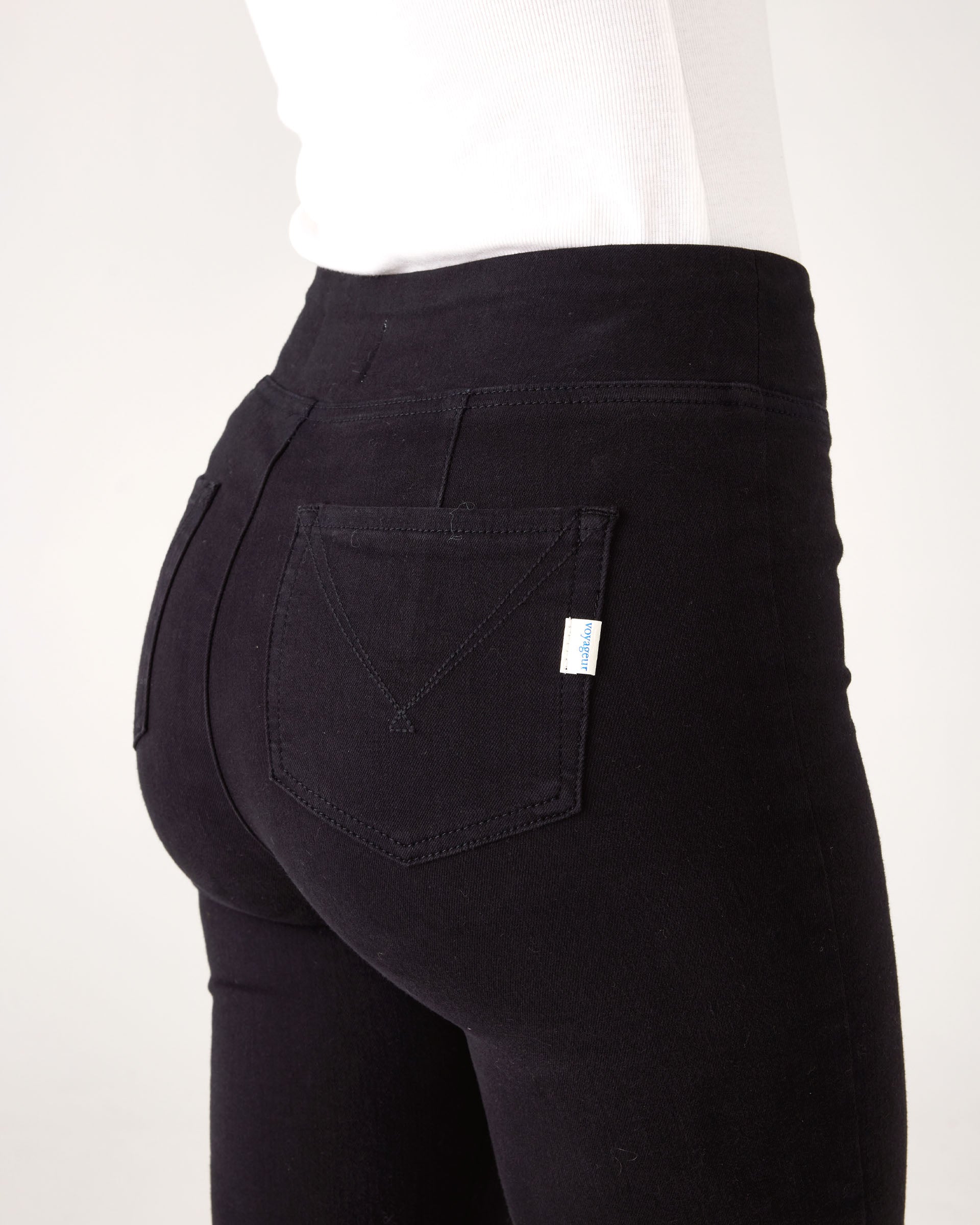 Close-up from behind: Woman wearing Mersea Nomad black ankle cigarette jeans, standing against a white background
