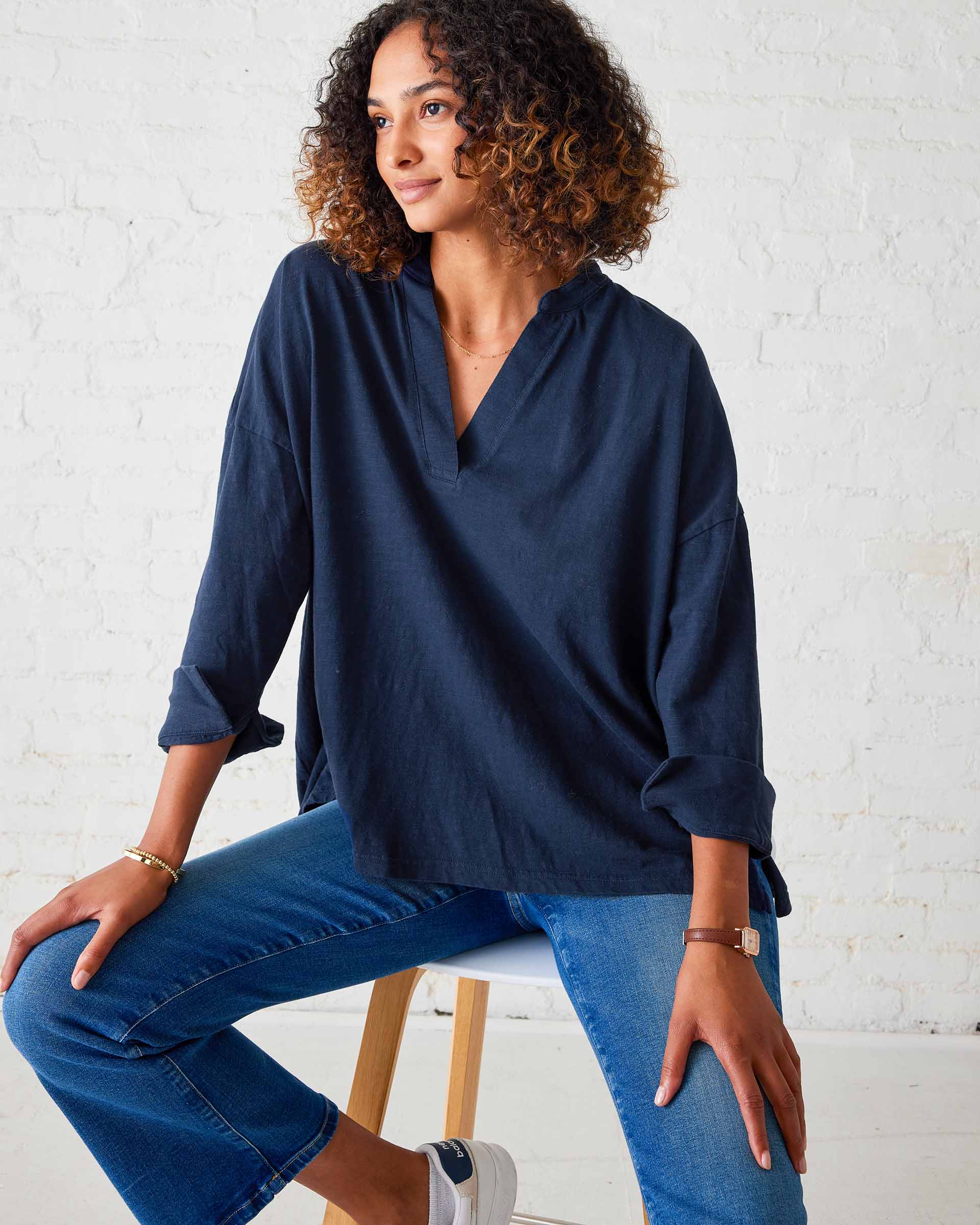 A woman wearing a long sleeve purple Amelia Cuff Tee with V-neck detail and white pants.