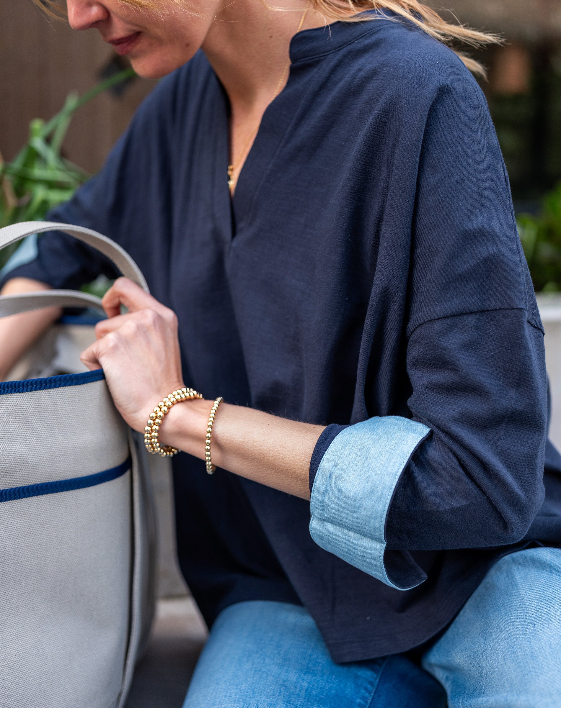 Person wearing a navy blue shirt with rolled-up sleeves, holding a gray bag.