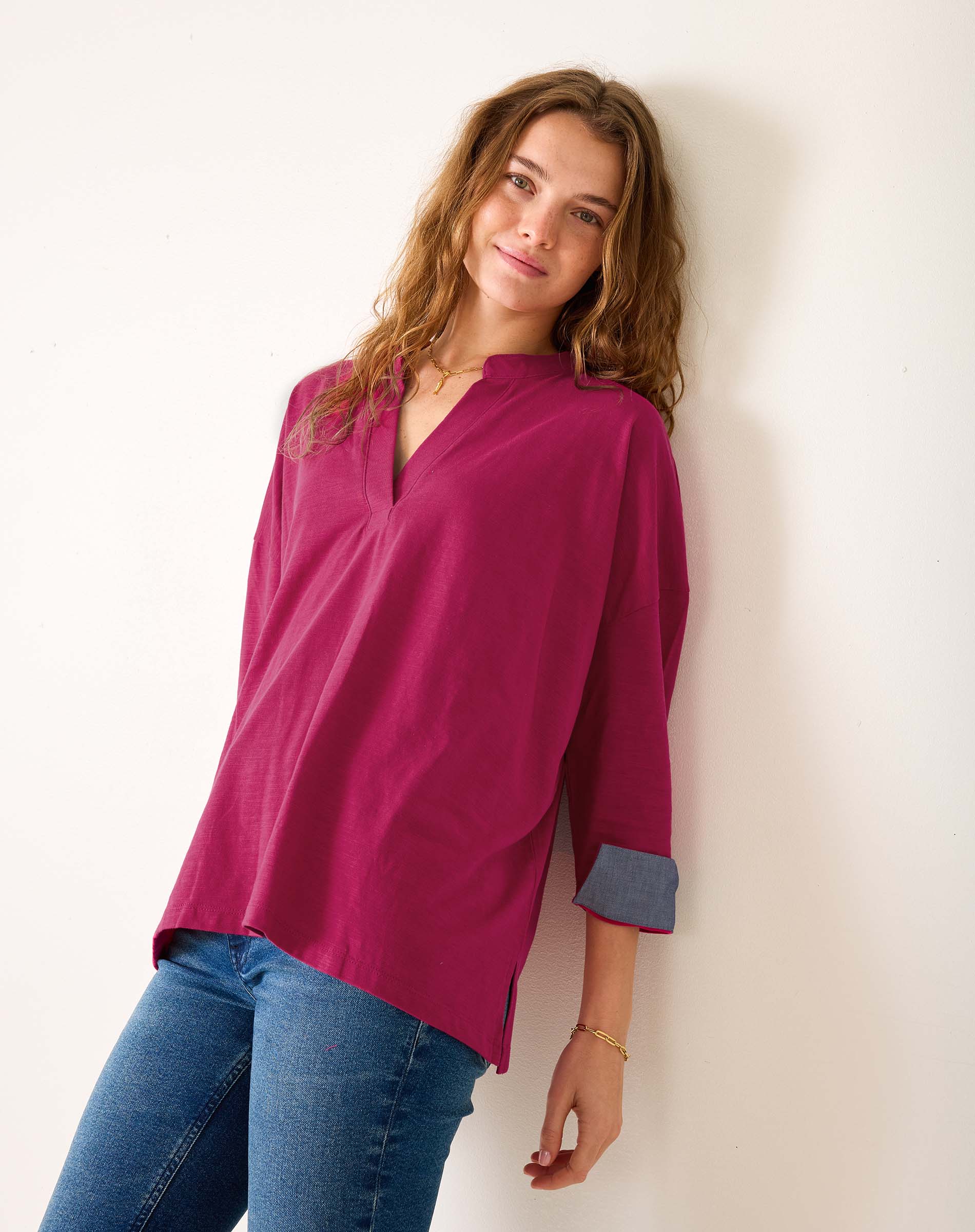 Woman wearing a magenta blouse and blue jeans against a white background