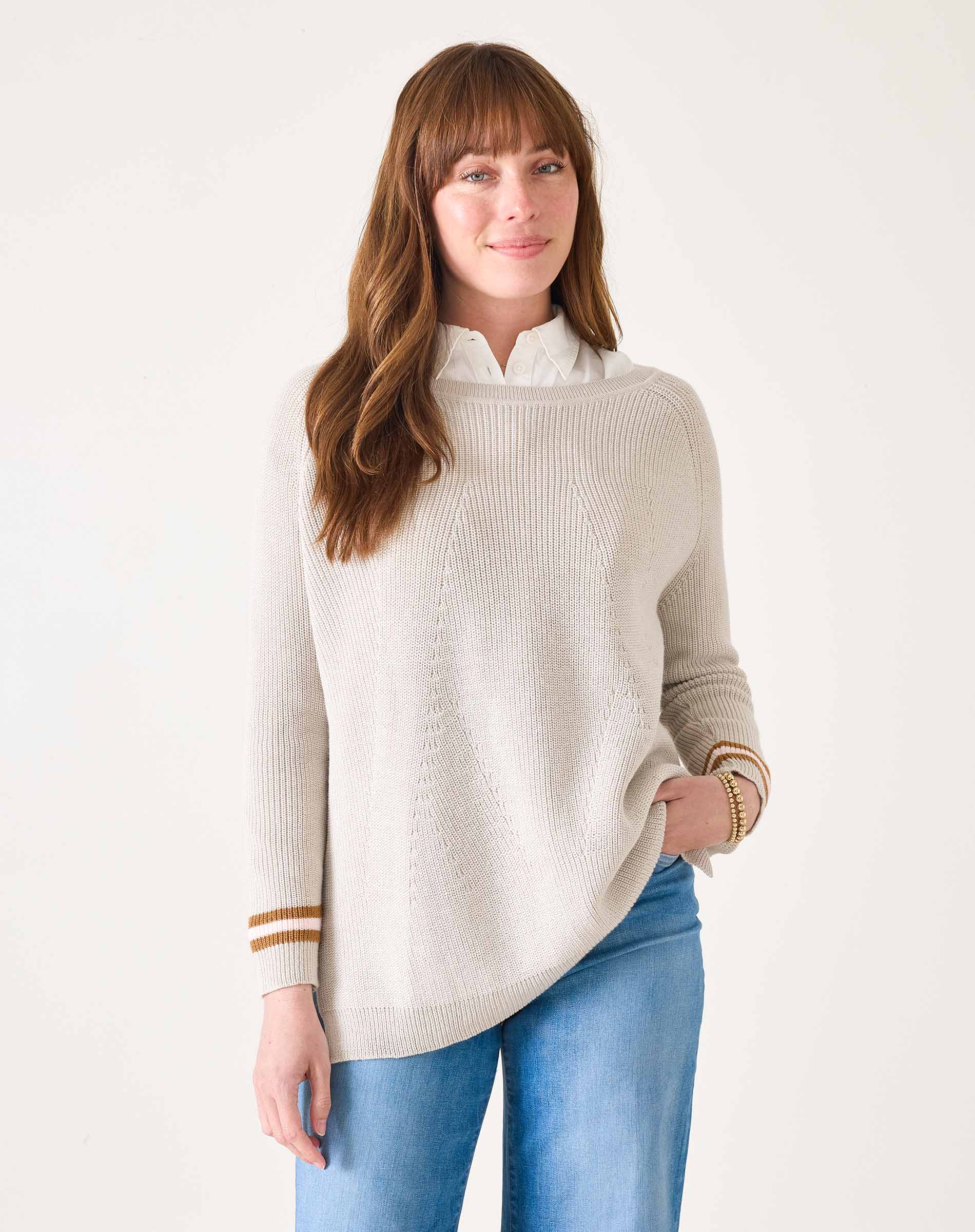 Woman wearing a beige sweater with gold trim and blue jeans on a white background