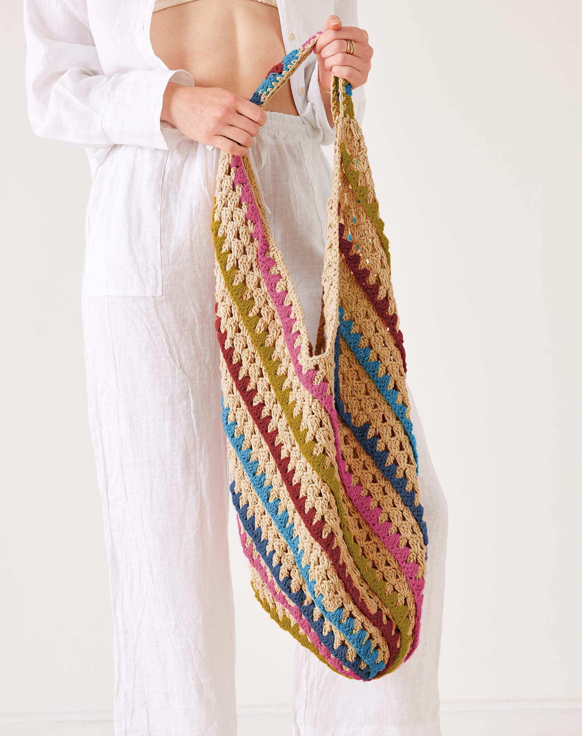 Person holding a colorful striped crochet bag against a white background