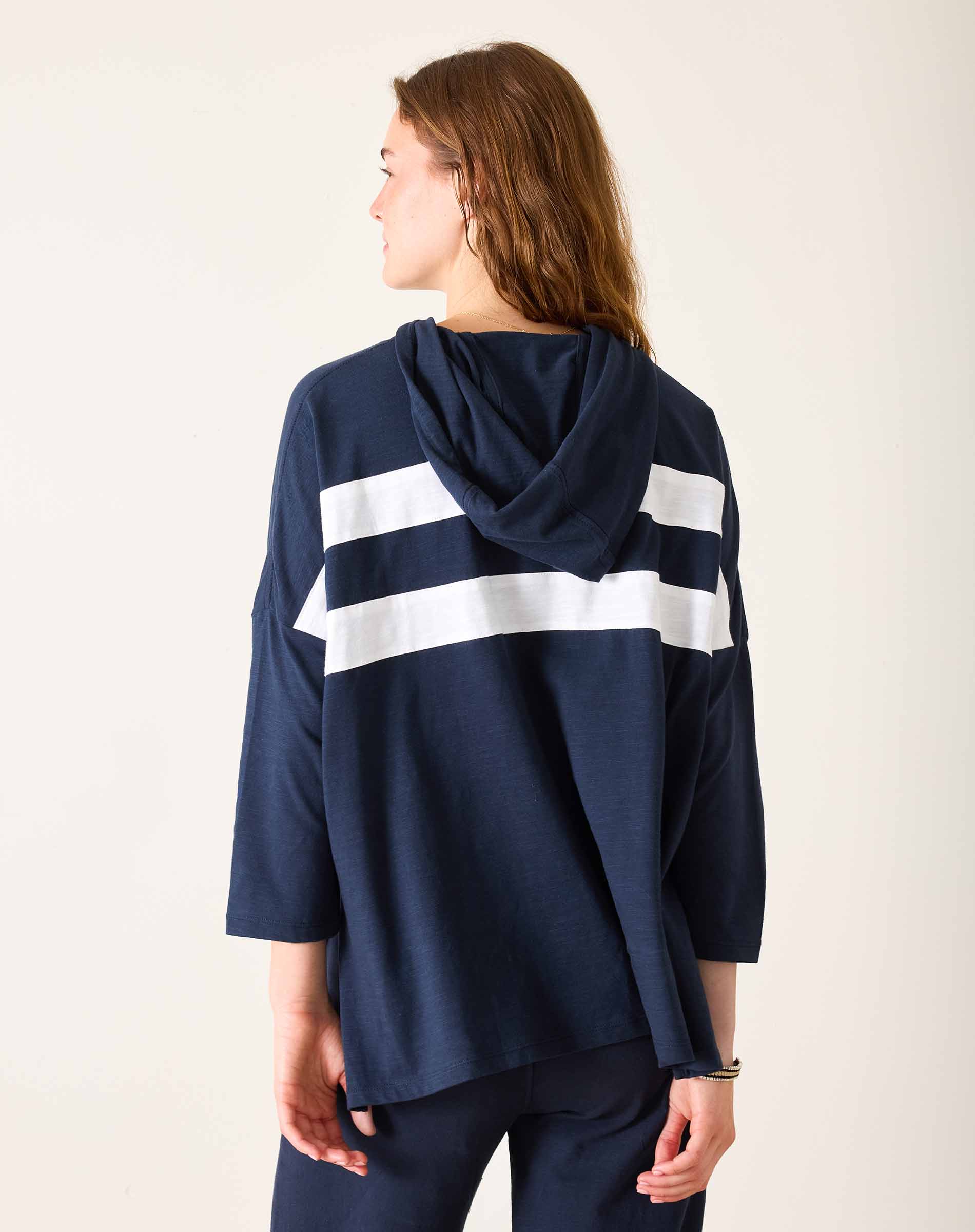 Person wearing a navy blue hoodie with white stripes from behind on a light background