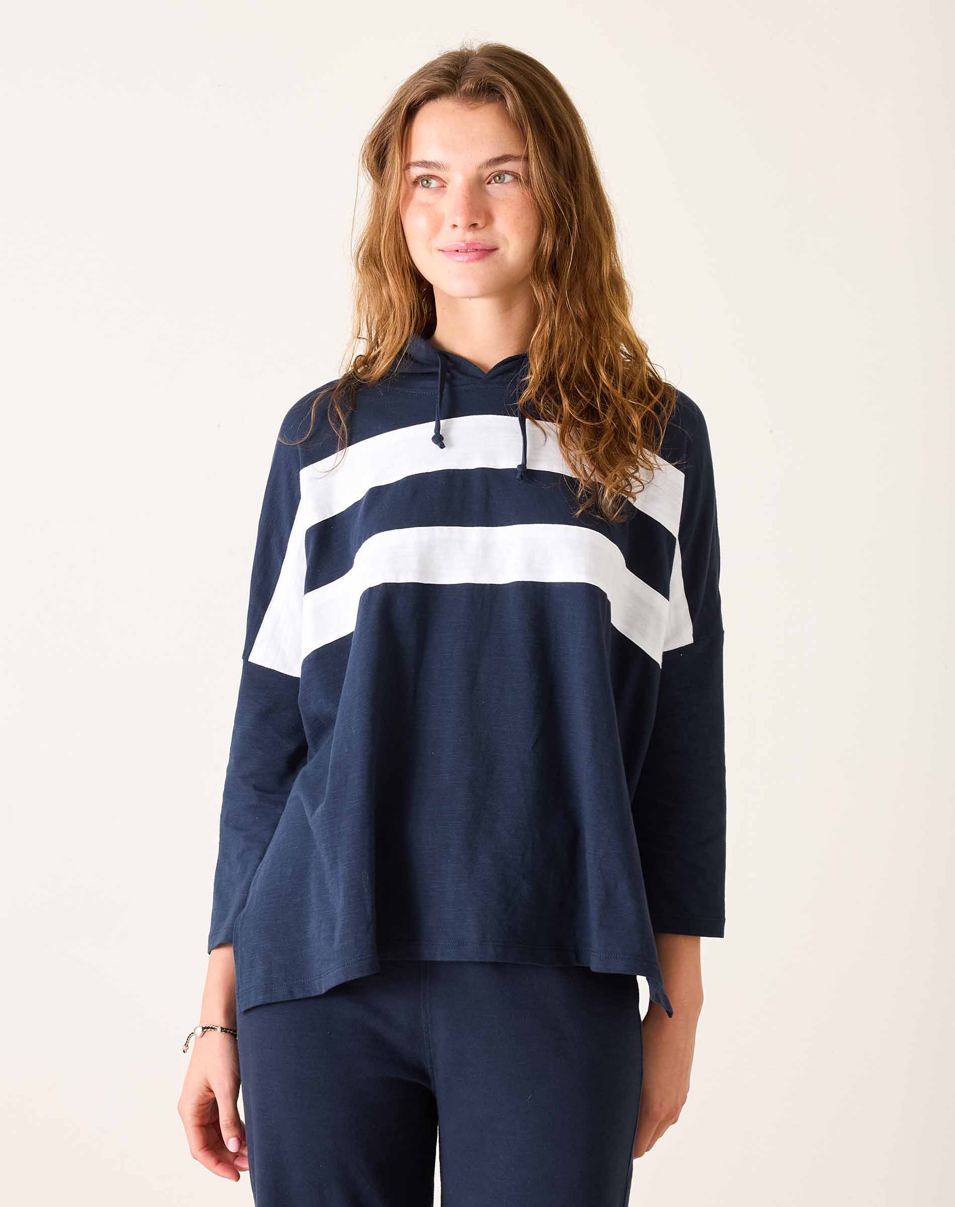 Woman wearing a navy blue hoodie with white stripes on a plain background