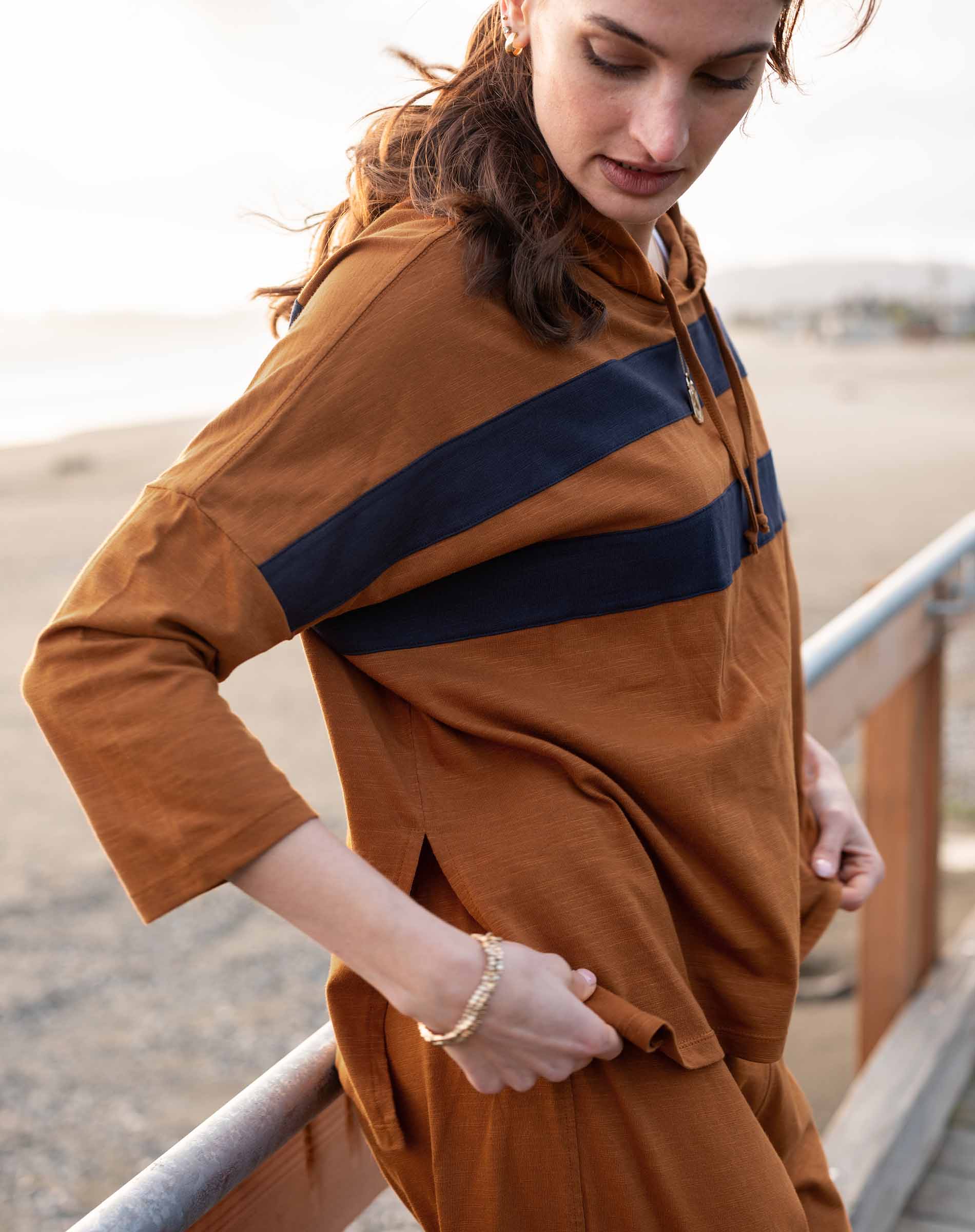 Woman wearing a brown dress with a blue stripe, standing outdoors.