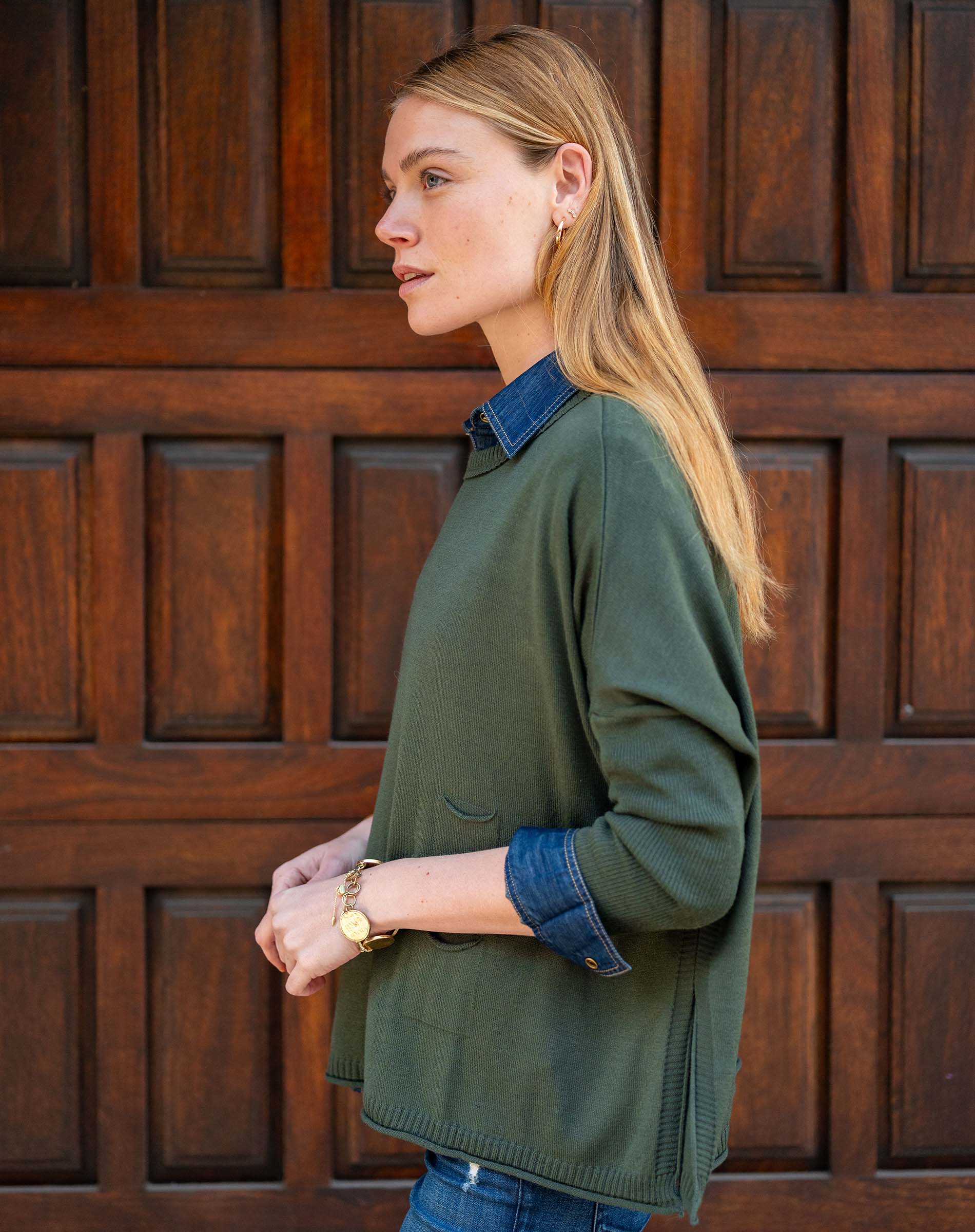 Woman wearing a green sweater and blue shirt against a wooden door background