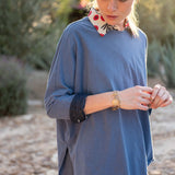 Woman wearing a blue long-sleeve top with a blurred natural background