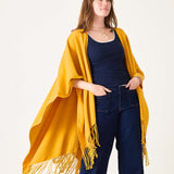 Woman wearing a yellow fringed poncho over a dark top and jeans on a white background