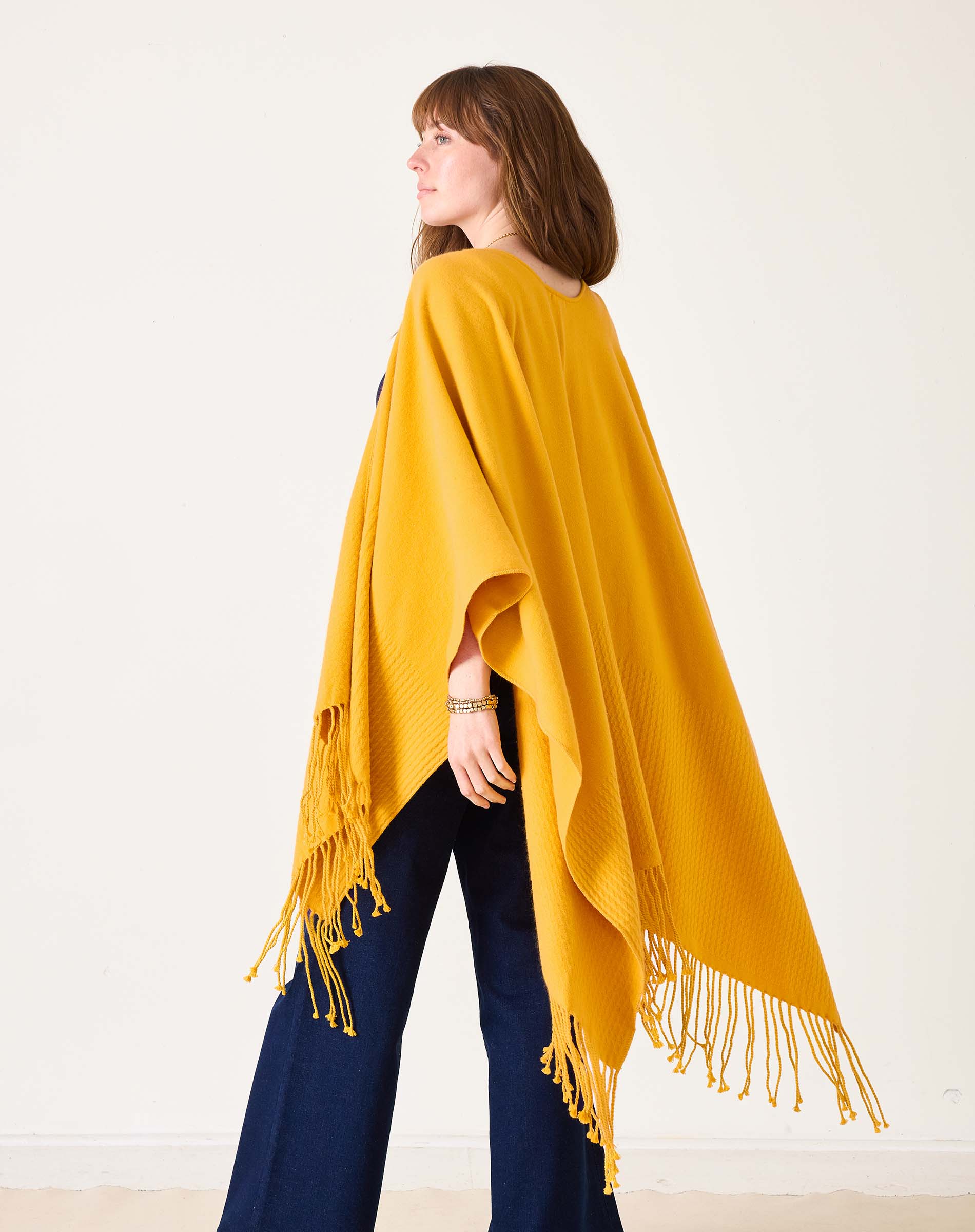 Woman wearing a yellow poncho with fringe on a white background
