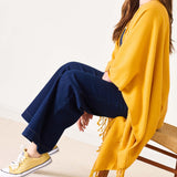 Person wearing a yellow cardigan, blue pants, and yellow sneakers sitting on a chair.