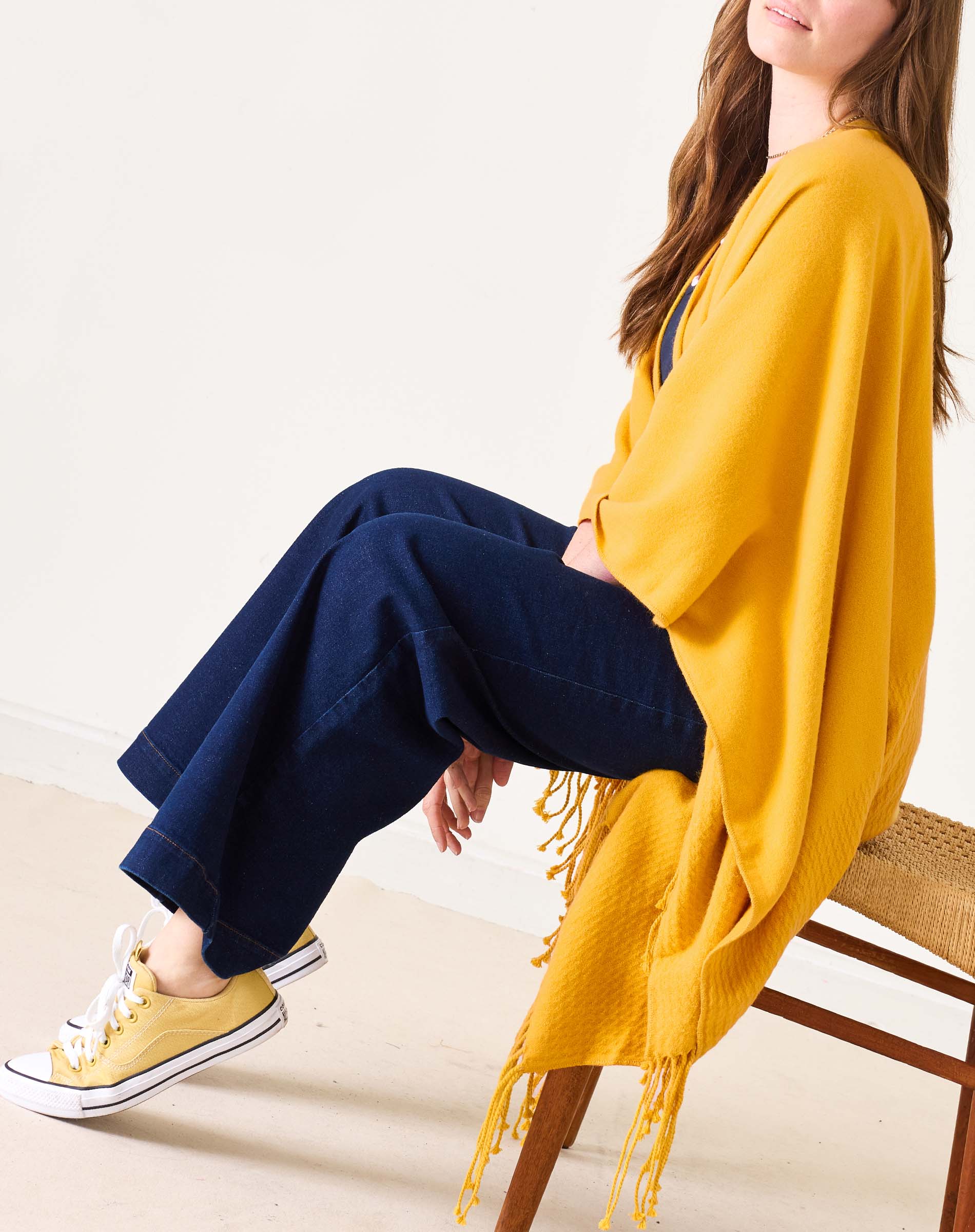 Person wearing a yellow cardigan, blue pants, and yellow sneakers sitting on a chair.