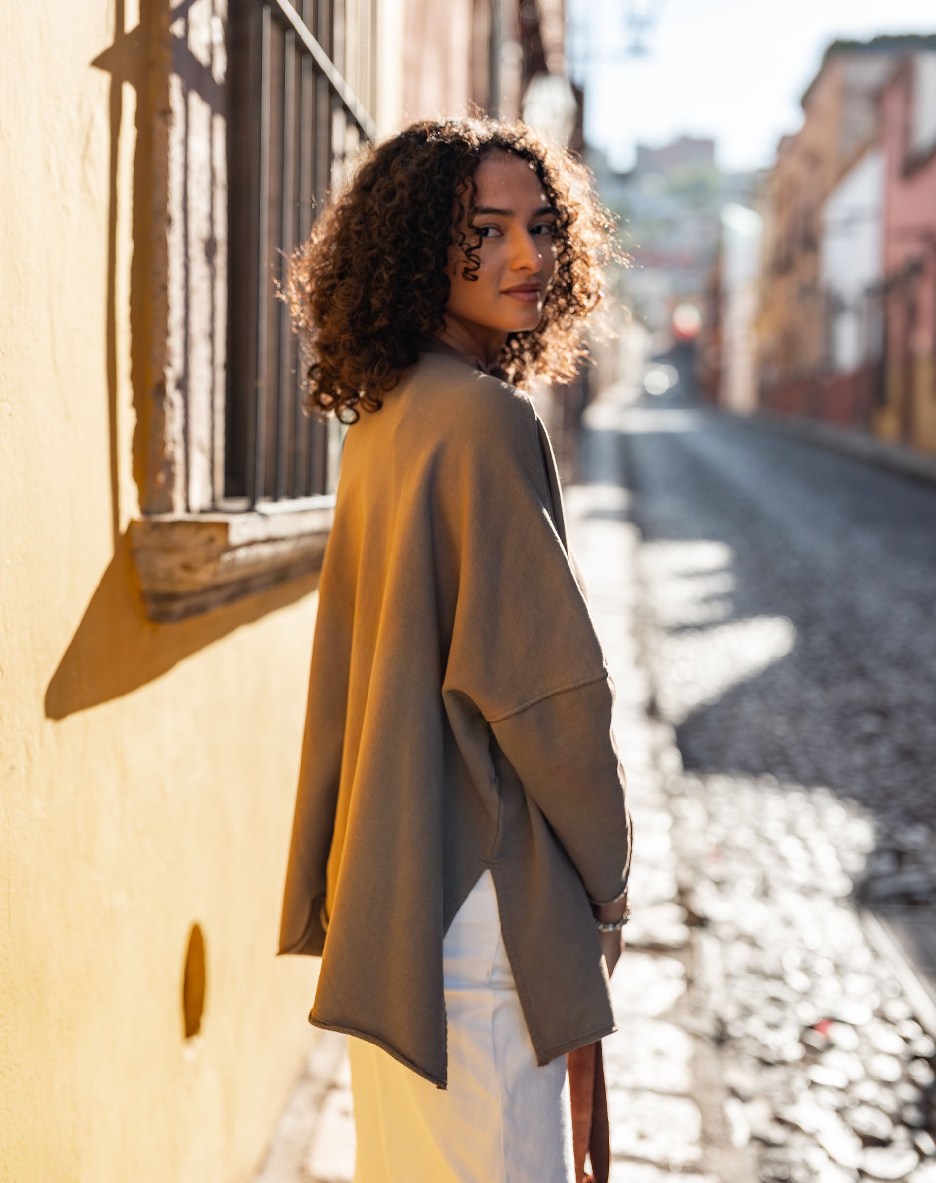 Woman standing on a sunlit street with a yellow wall