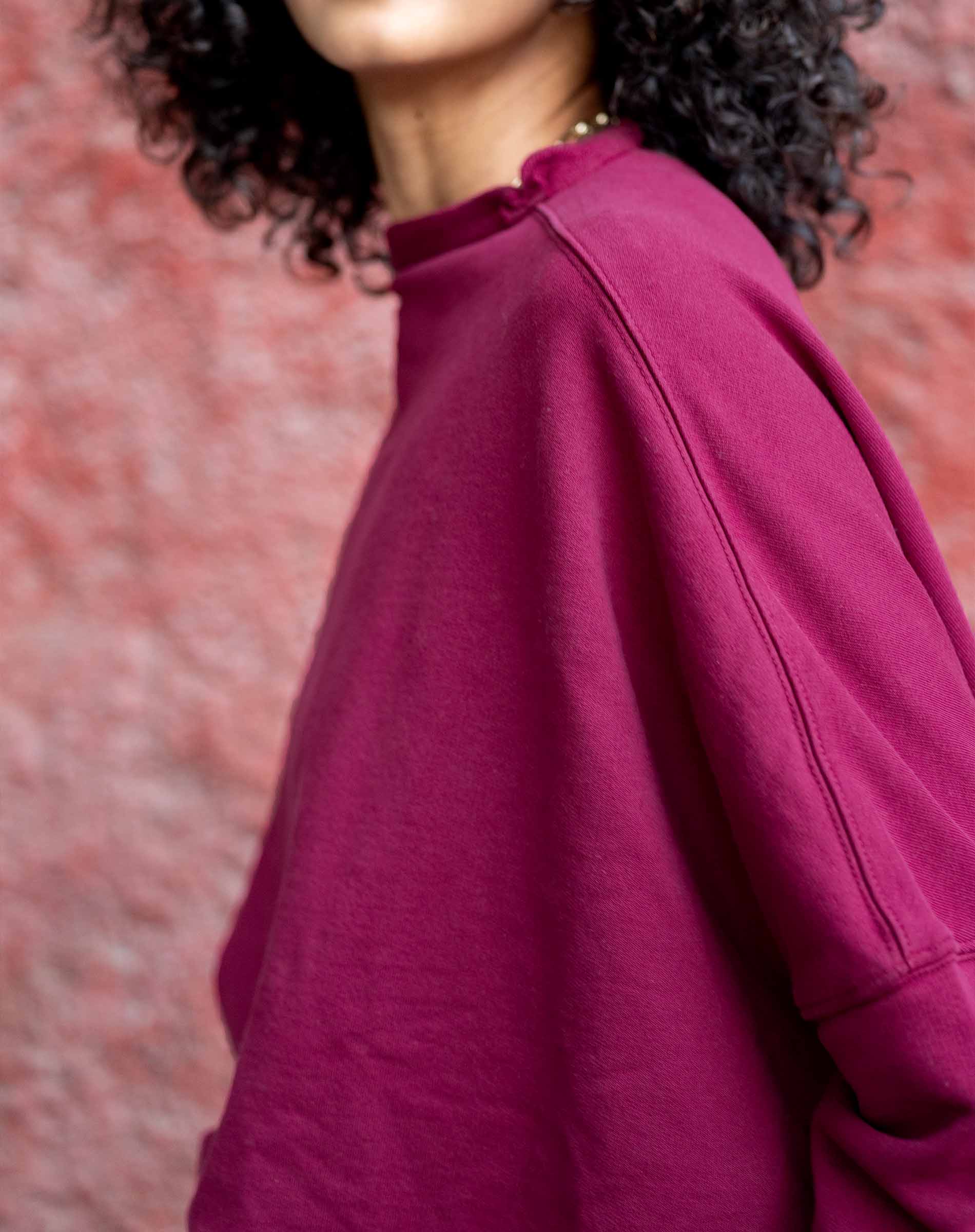 Person wearing a magenta sweater against a red brick wall