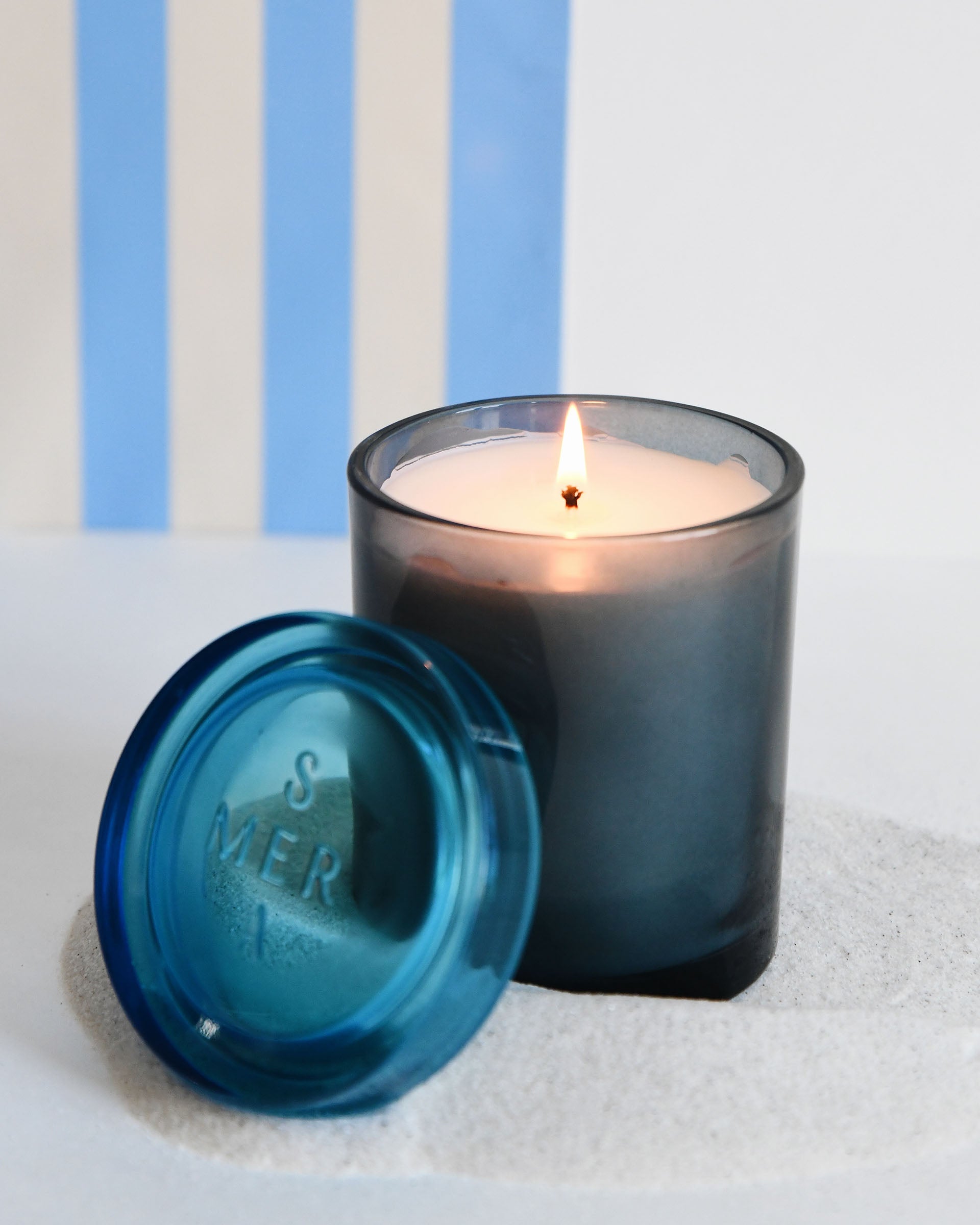 joli jar candle lit with a blue striped backdrop