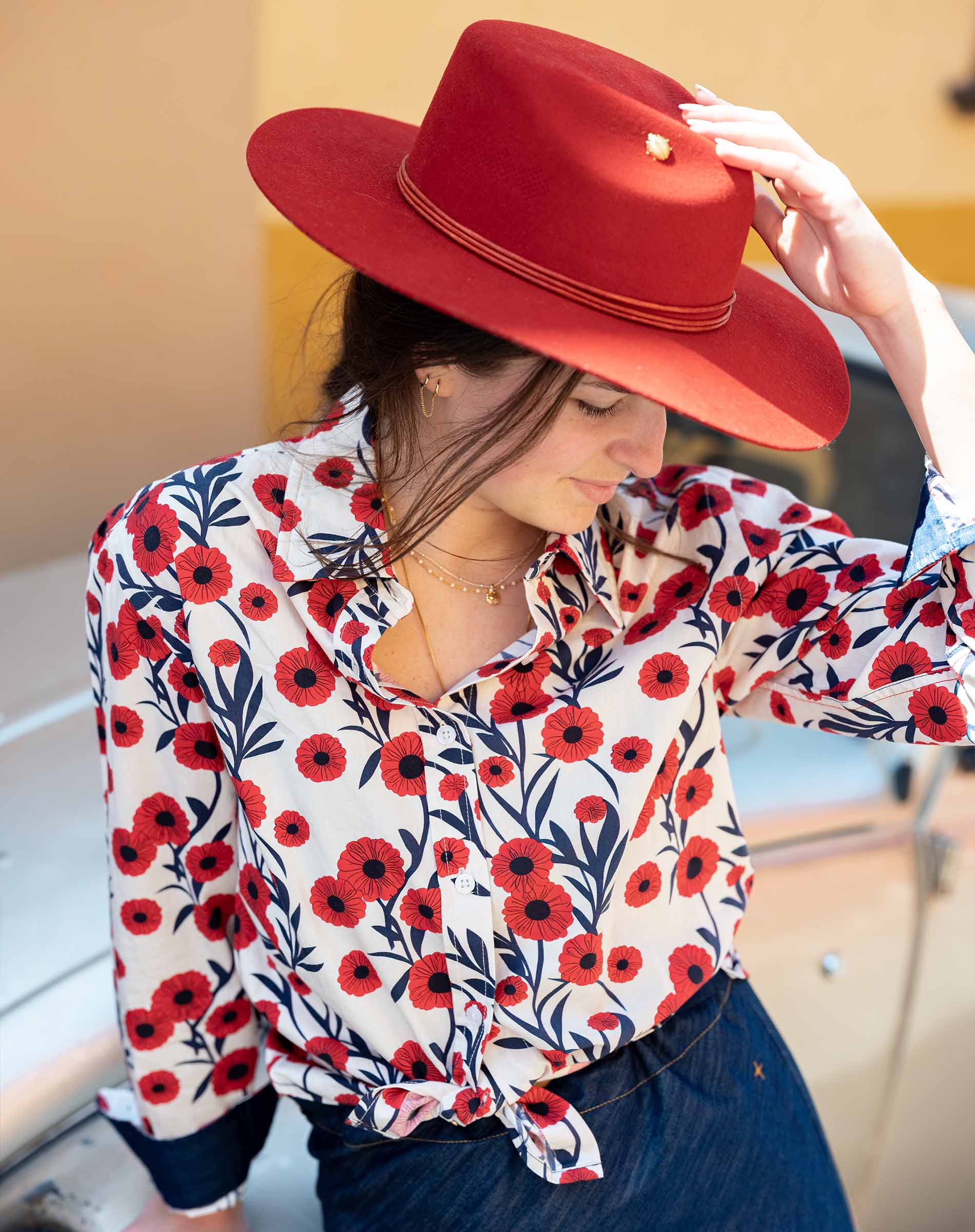Woman wearing a red floral blouse and large red hat, sitting on a bench.