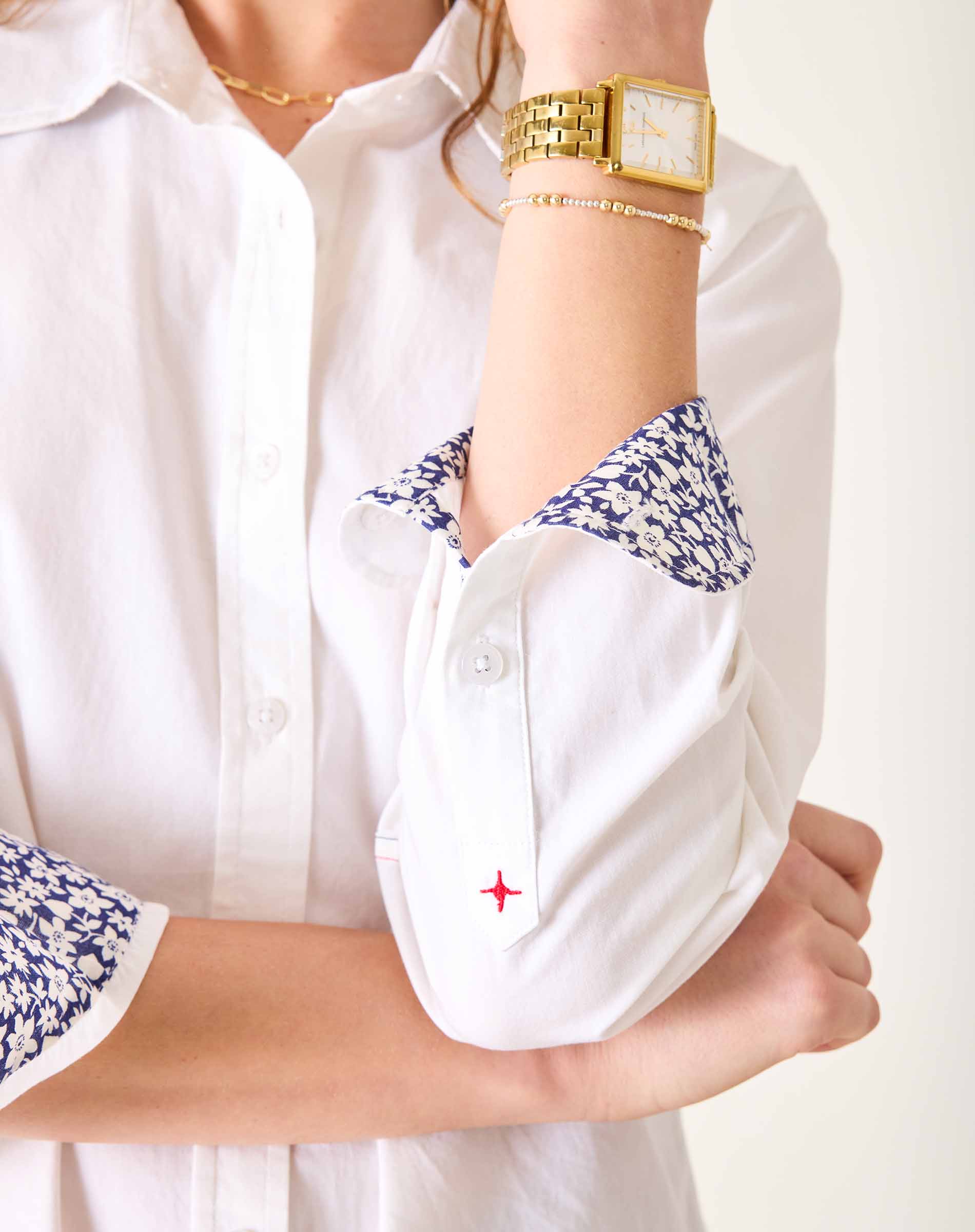 Close-up of a person wearing a white shirt with floral cuffs and a gold watch.