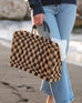 female holding medium sized straw bag with navy leather handles and a navy checkered print on beach