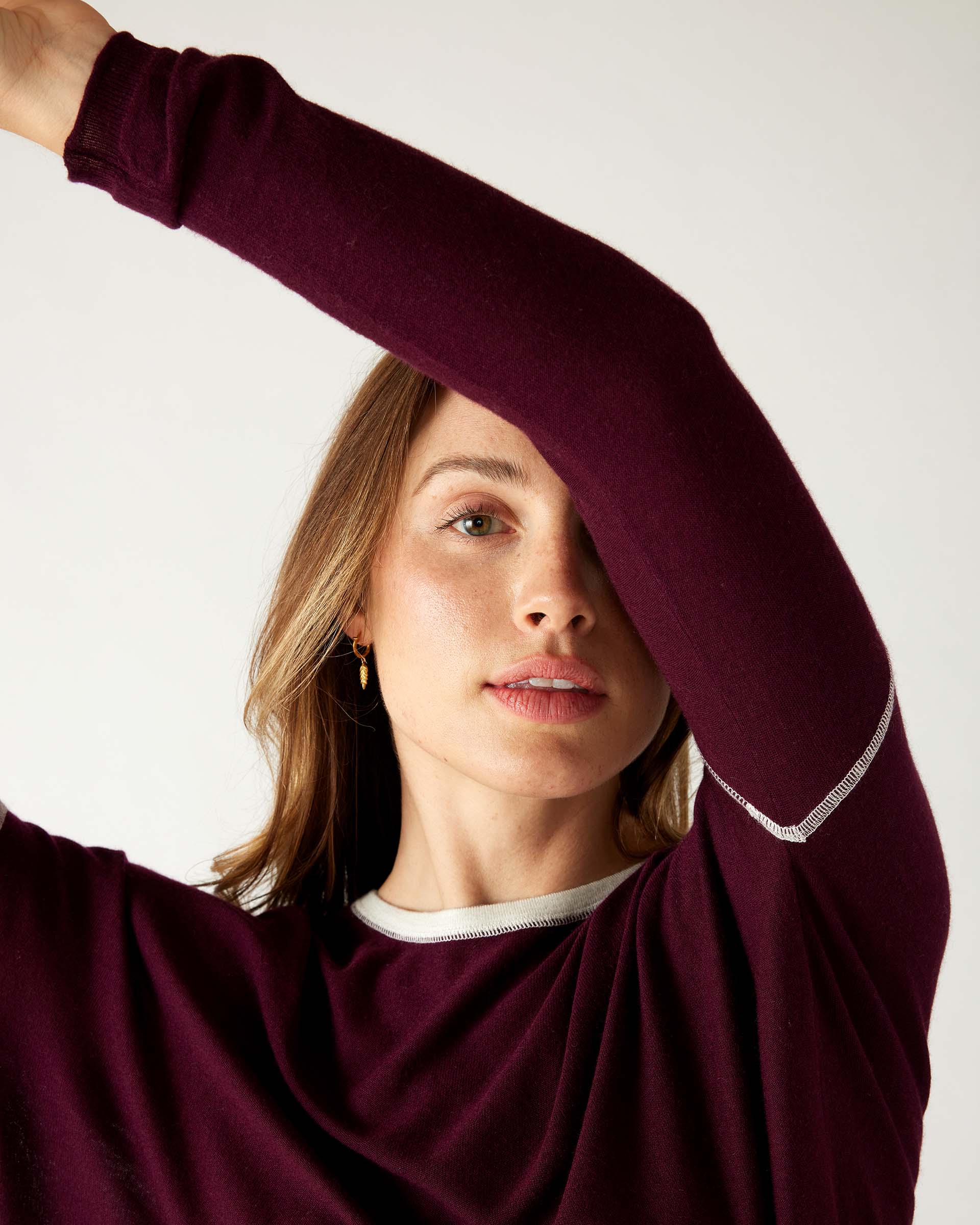 woman wearing mersea saltwash sweater in cabernet red with arms rsaised