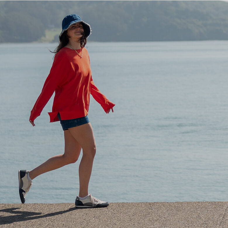 Person in a red sweater and blue hat walking by a body of water.