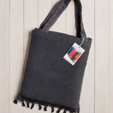 dark grey beach bag with fringe at the bottom on a white wood background