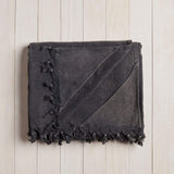 folded dark grey beach blanket with fringe on a white wood background