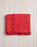 folded red beach blanket with fringe on a white wood background