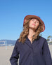 female wearing red straw wide brim hat with opening on top and red trim looking at sky at the beach