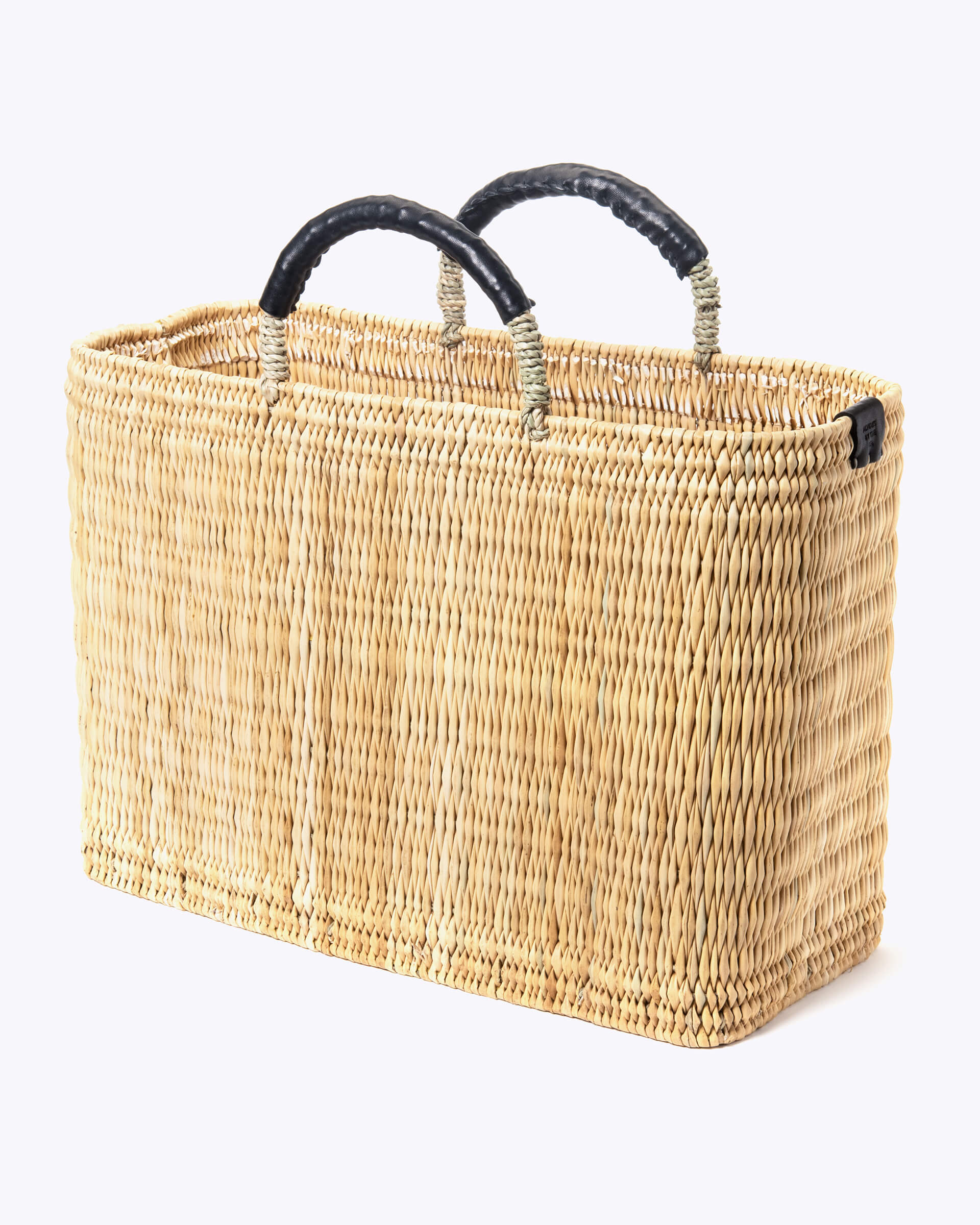 large straw basket wrapped with black leather handle on a white background at an angle