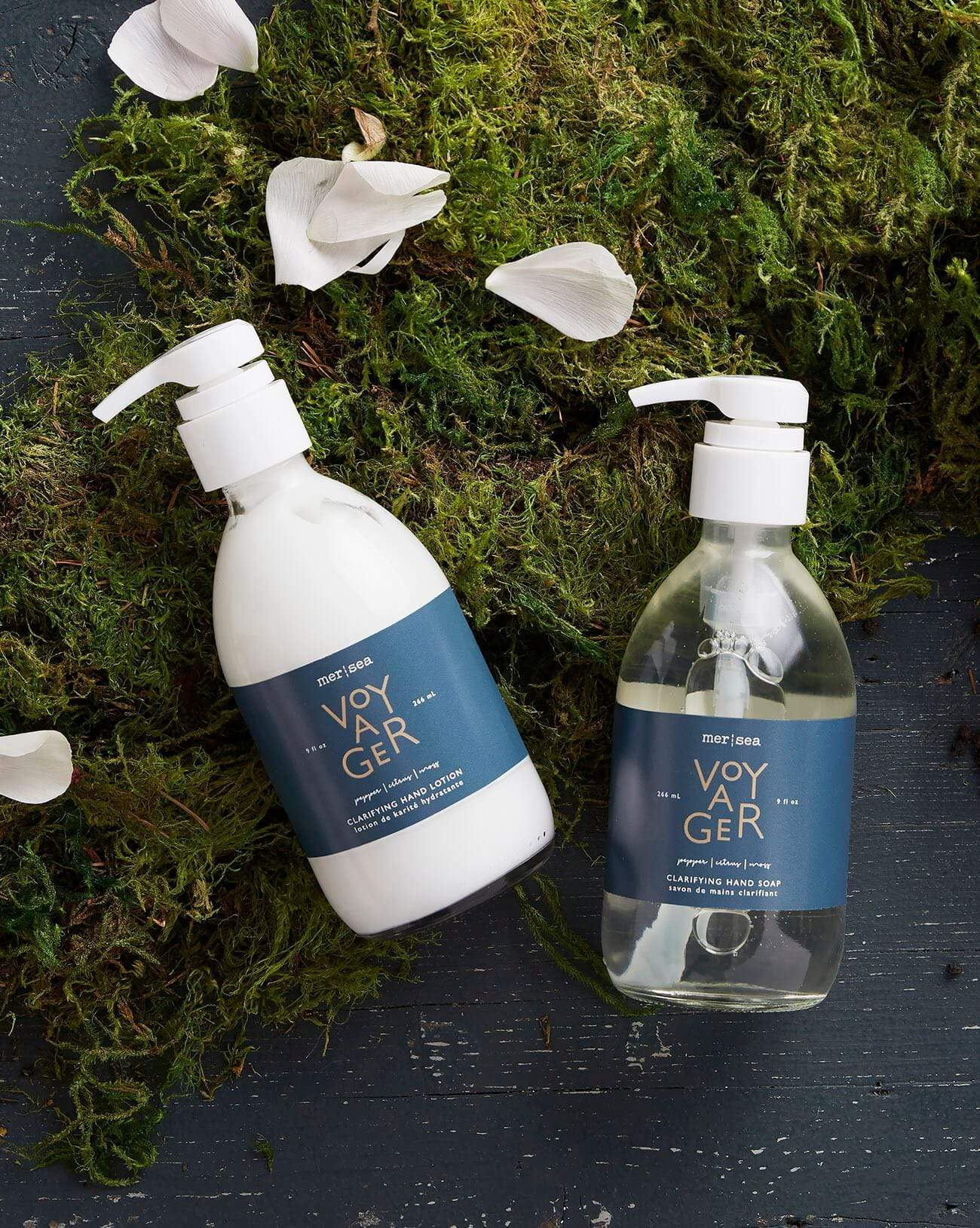 two 9 oz bottles of Voyager shea lotion and hand soap laying on top grass and a blue background