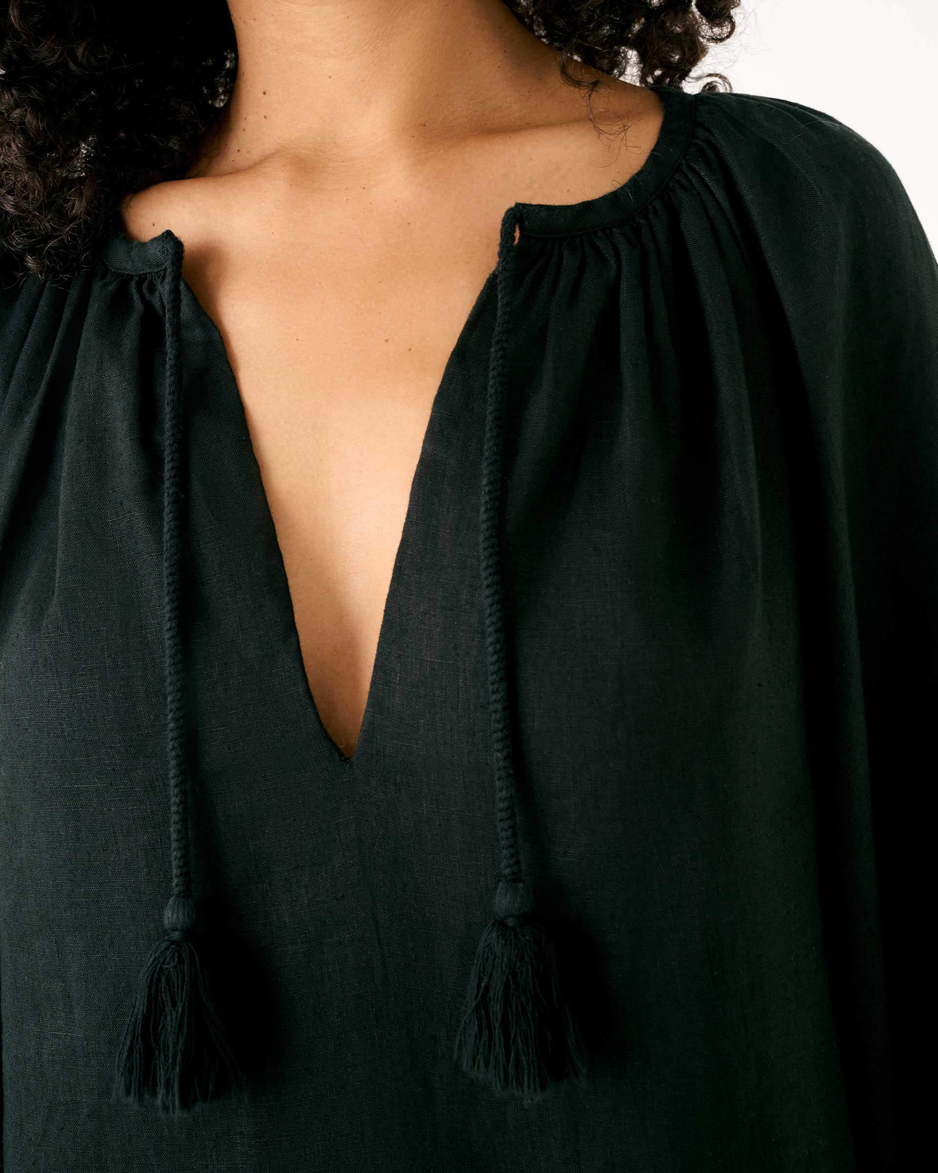 female wearing black split v neck linen dress with tassel ties close up