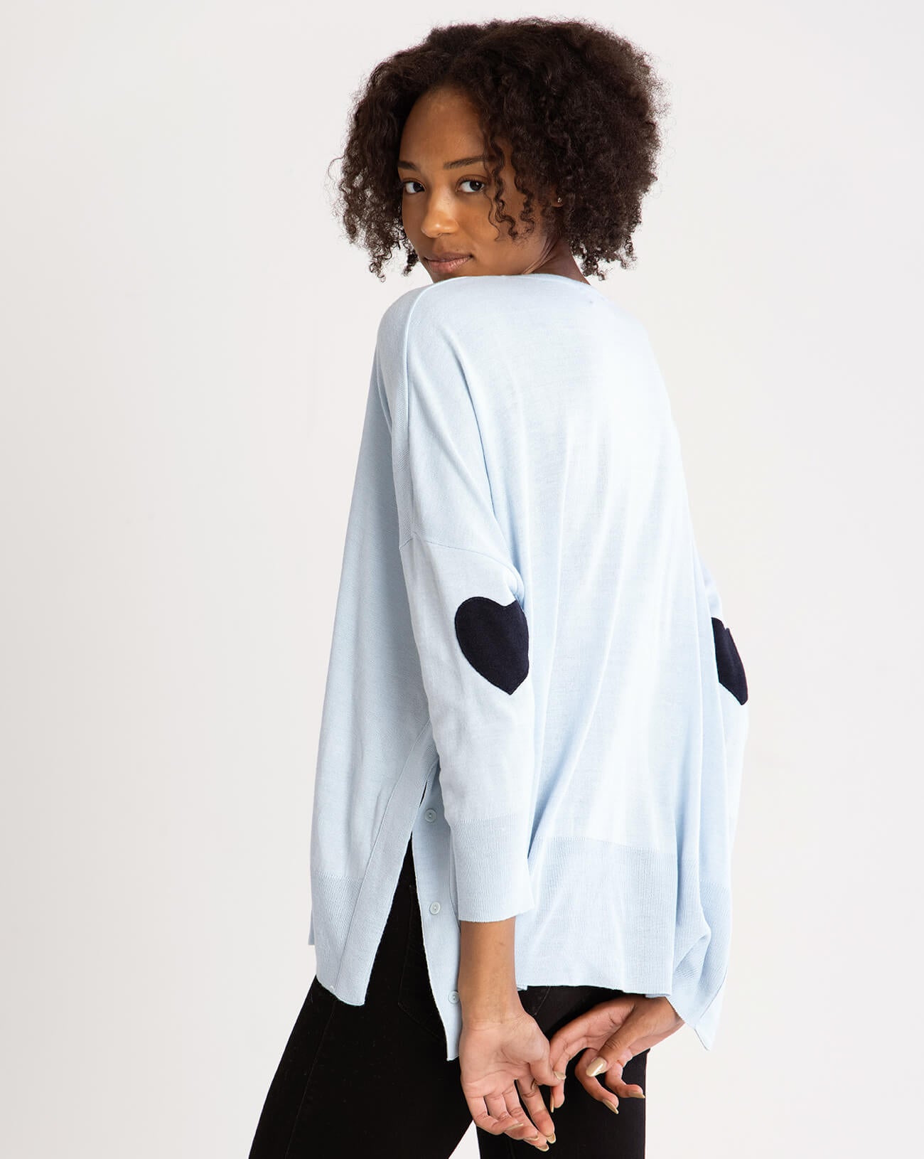 rearview of female wearing light blue sweater with blue  heart elbow patch on white background