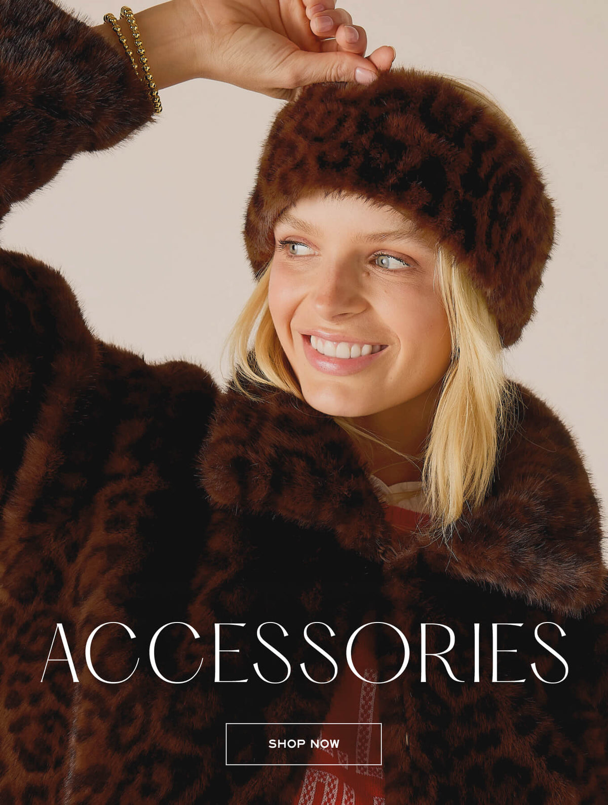 A woman wearing a plush, faux-fur animal print hat and a matching oversized wrap, smiling. Text: 'ACCESSORIES SHOP NOW'