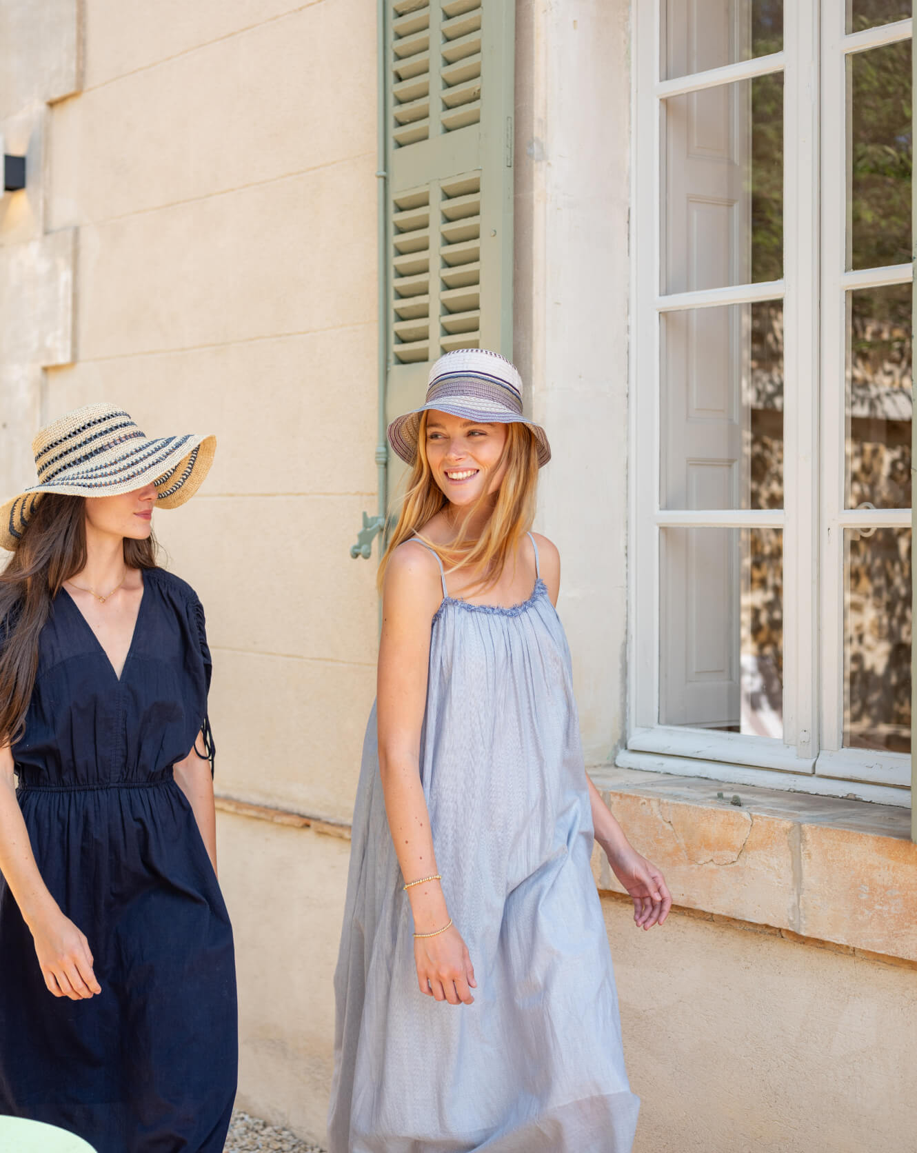 Two women wearing hats standing in front of a building with a window.