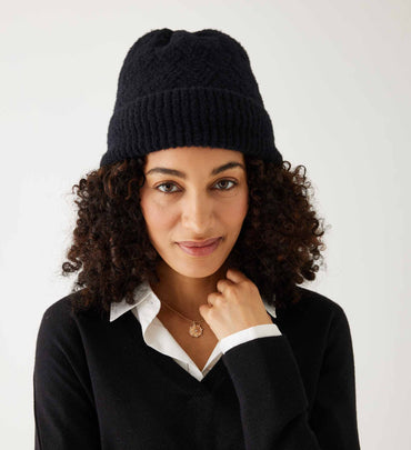 female wearing black beanie and white v neck sweater over a collared shirt on a white background