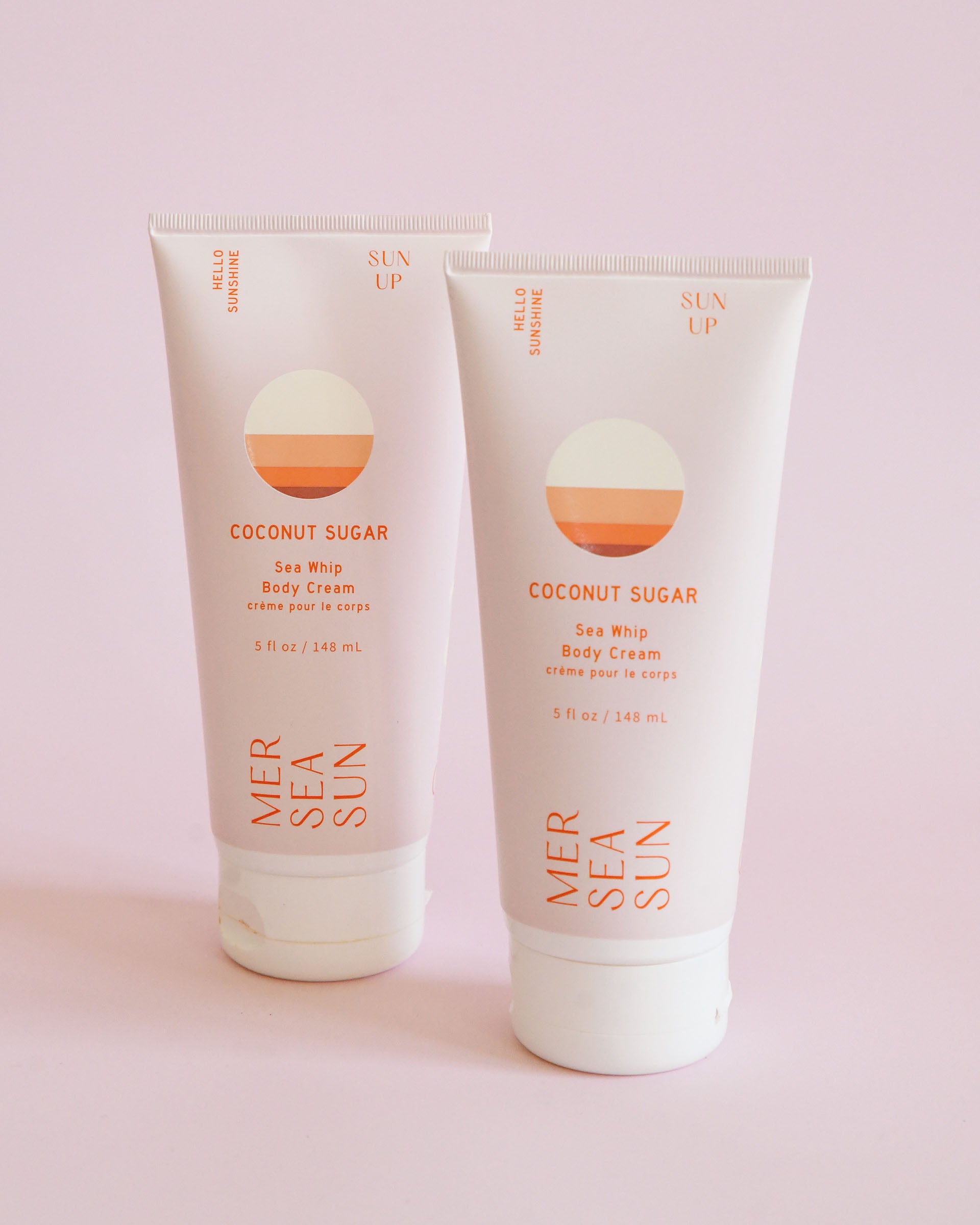 Coconut Sugar Sea Whip Body Cream MERSEA Sun. Two Pink and orange tubes stand up in front of pink background.