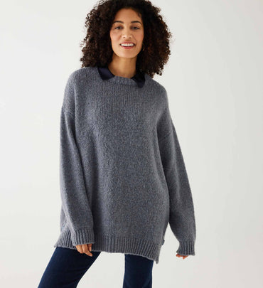 female wearing grey sweater over dark wash jeans on a white background