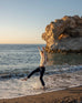 Women wearing a sea salt Mersea Beachside Turtleneck sweater dancing on beach in front of water