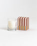 Pumpkin Whimsea candle in glass votive next to striped box on a white background