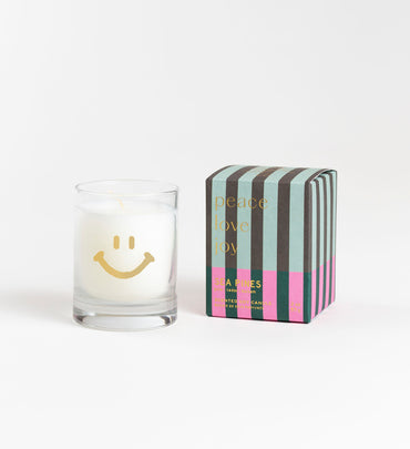sea pines glass white candle with gold smiley face next to striped box