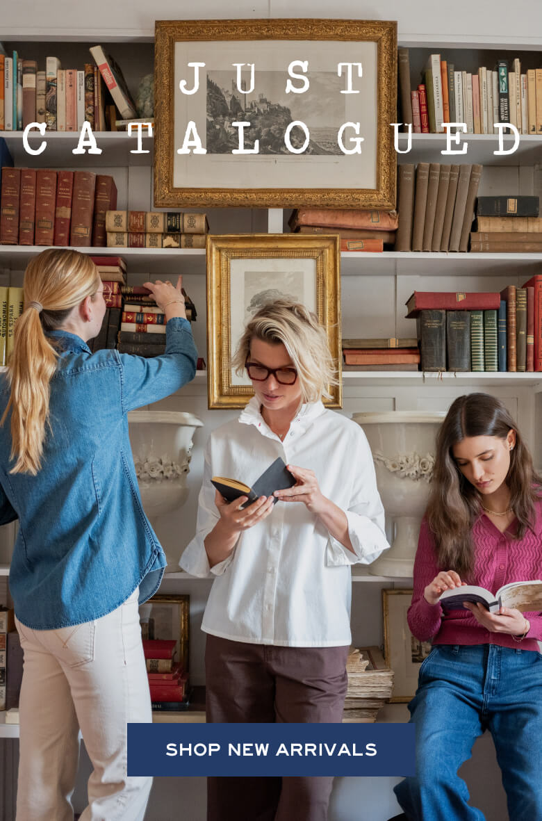Promotional banner featuring three women in a library setting reading books, with a large framed painting of a landscape. Text: 'JUST CATALOGUED' and 'SHOP NEW ARRIVALS'