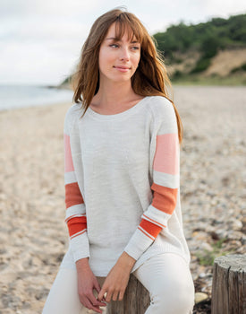 female wearing pink striped sweater sitting on a stoop at the beach