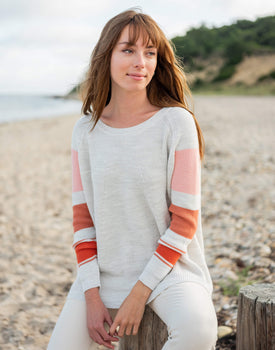 female wearing white sweater with pink color blocks sitting on the beach 