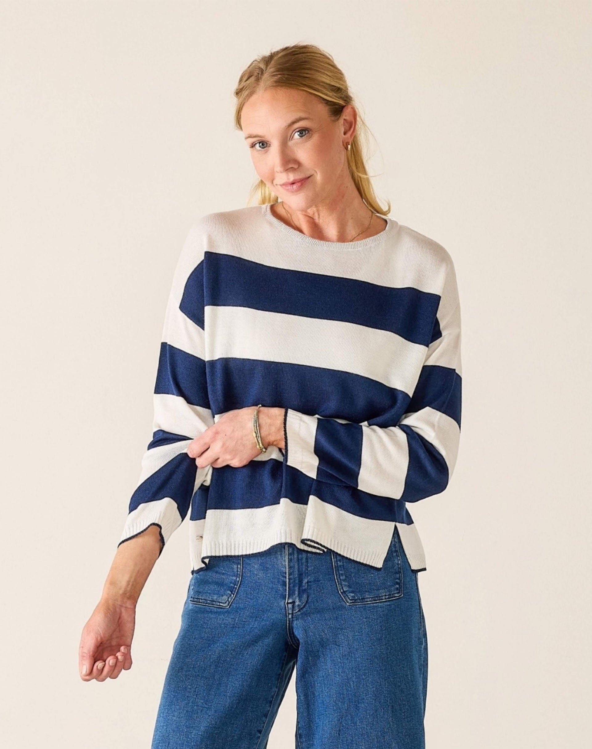 Woman wearing a blue and white striped sweater with blue jeans on a plain background