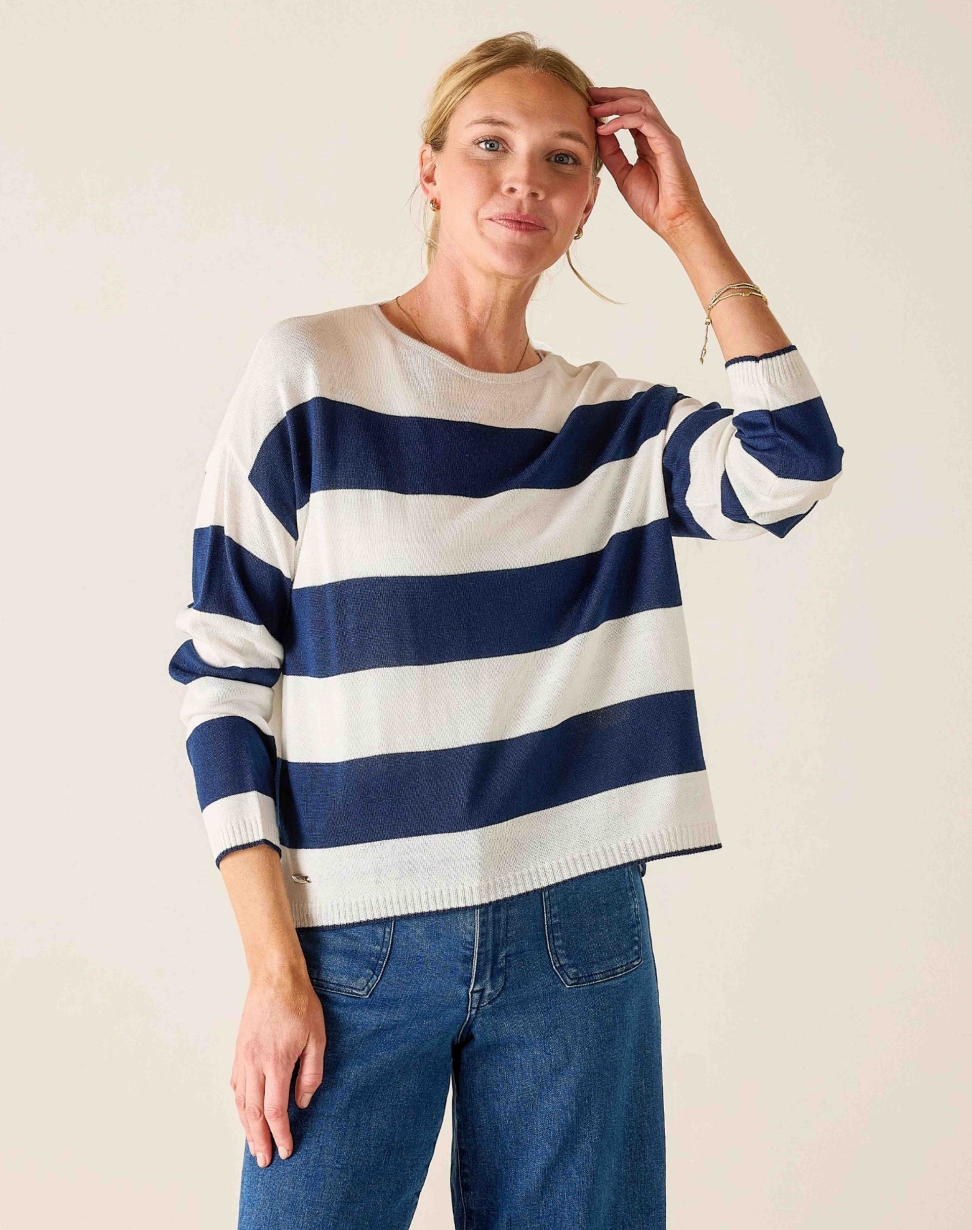 Woman wearing a blue and white striped sweater with blue jeans against a plain background