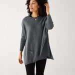 female wearing mersea storm catalina sweater touching her hair standing against a white background