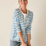 Woman wearing a blue and white striped shirt holding a hat against a plain background