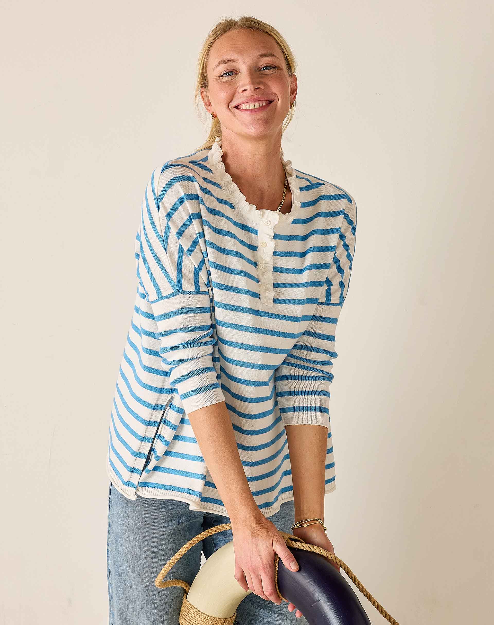 Woman wearing a blue and white striped shirt holding a hat against a plain background