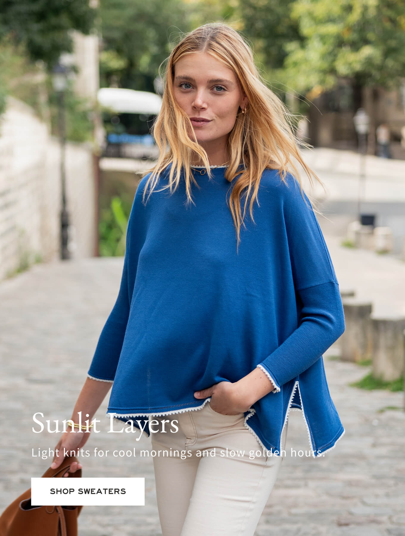 Sunlit Layers - Light knits for cool mornings and slow golden hours. - Image of a woman wearing a blue sweater with white trim detail.