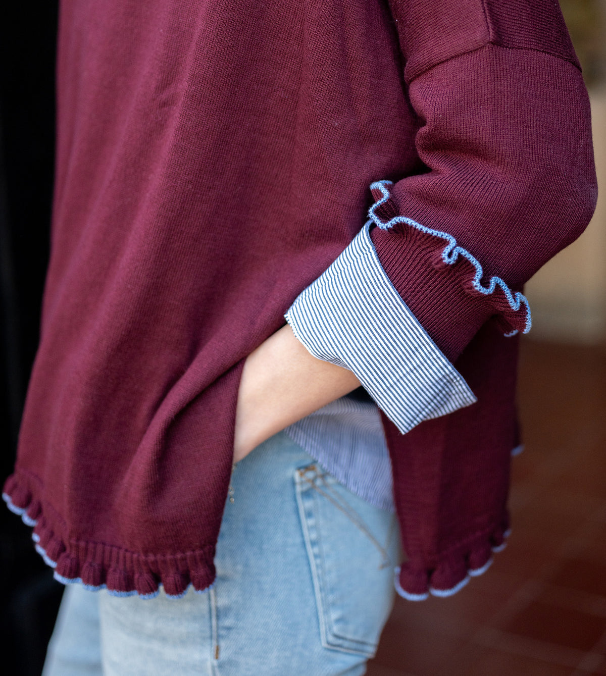 Burgundy knit sweater featuring a ruffled hem and layered stripe detail.
