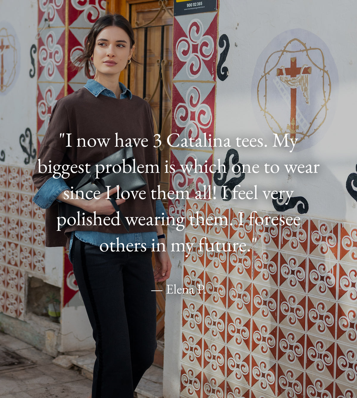 A woman standing in front of a wall of Mediterranean-style tiles with an overlaid testimonial quote from Elena P. Text: "I now have 3 Catalina tees. My biggest problem is which one to wear since I love them all! I feel very polished wearing them. I foresee others in my future." — Elena P.
